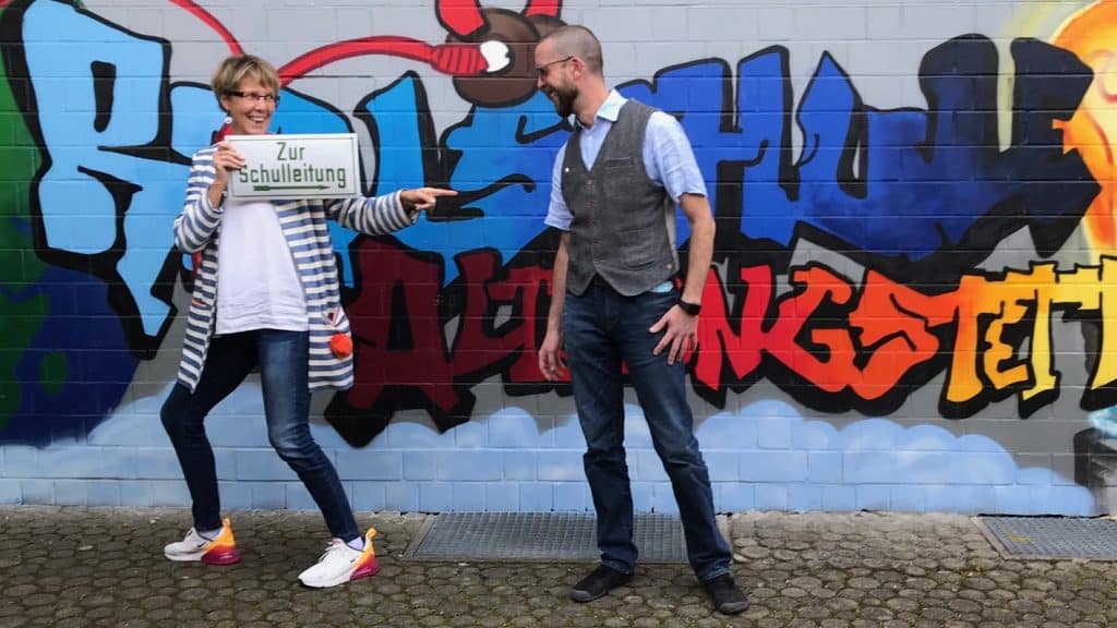 Zwei erwachsene Personen scherzen vor einem bunten Graffiti