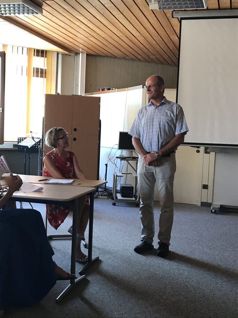 Eine stehende Person spricht zu einer sitzenden Person in einem Klassenzimmer